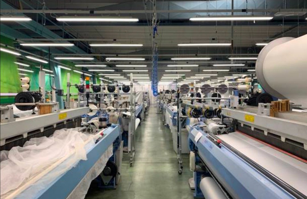 Reparto produttivo con lunghe file di telai industriali e plafoniere a soffitto