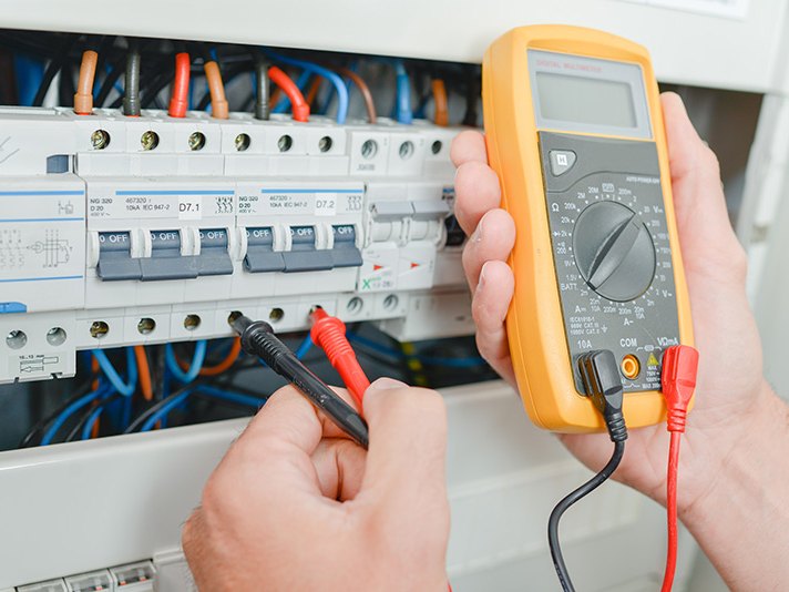 Tecnico che misura la tensione con un multimetro digitale su una fila di interruttori